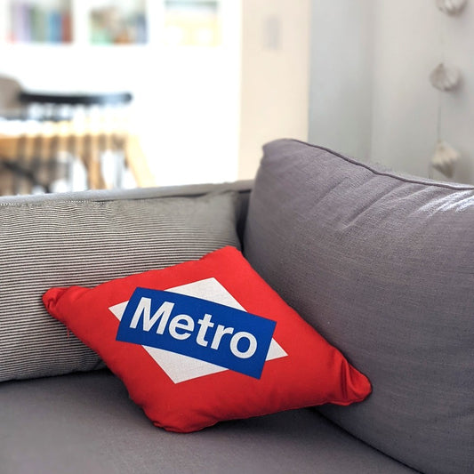 Cojín rojo con logo de Metro Madrid sobre sofá gris en sala moderna