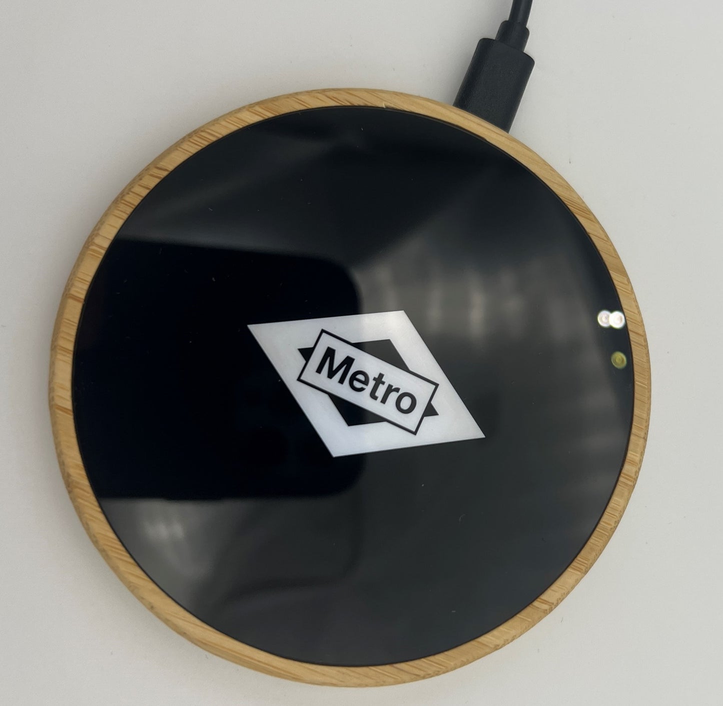 Cargador inalámbrico circular negro con borde de bambú y logo Metro sobre fondo blanco.