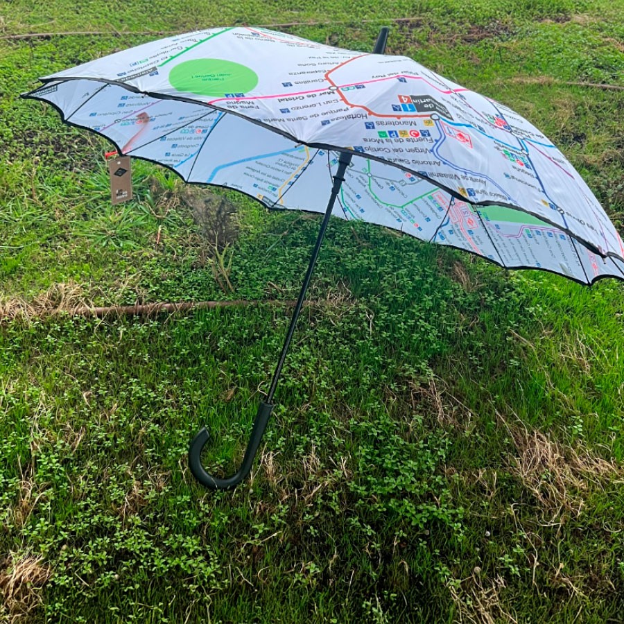 Paraguas con diseño de mapa del metro sobre césped verde, asa curva negra.
