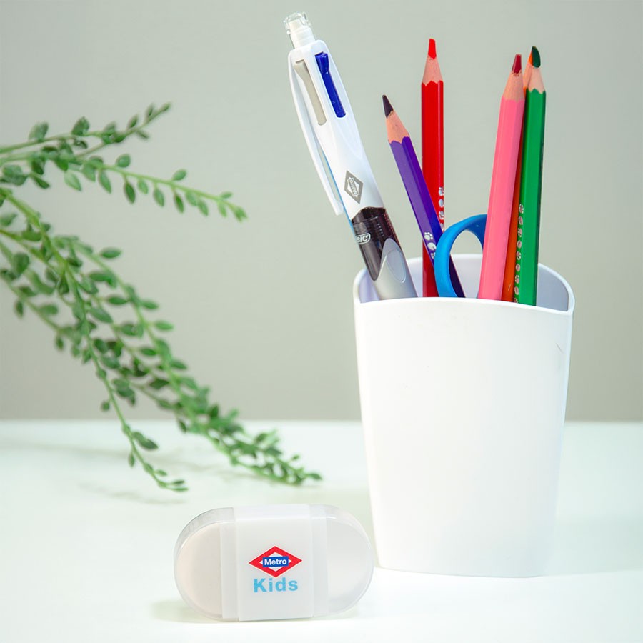 Vaso blanco con lápices de colores, bolígrafo y tijeras, borrador Metro Kids en un escritorio