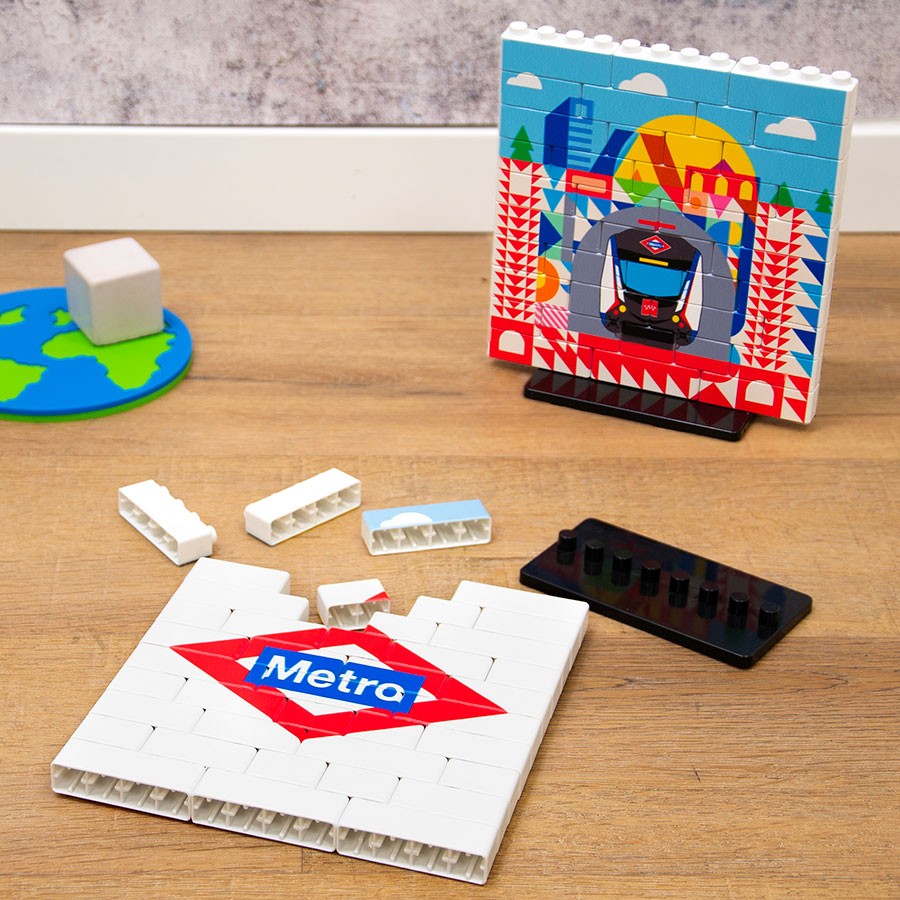 Set de bloques de construcción con logo de Metro de Madrid y fondo colorido sobre mesa de madera.