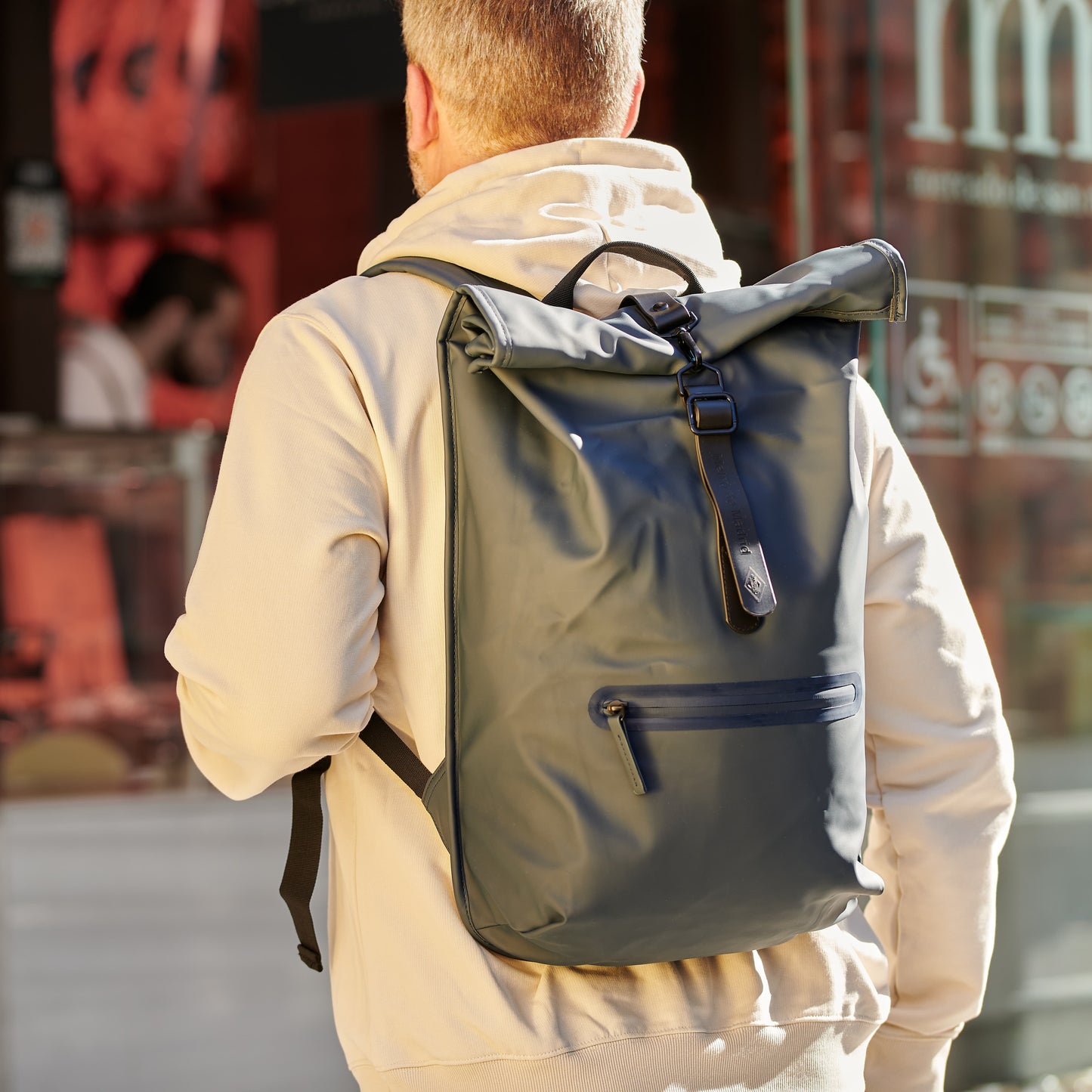 Hombre con mochila impermeable azul oscuro en la ciudad, chaqueta beige, fondo urbano