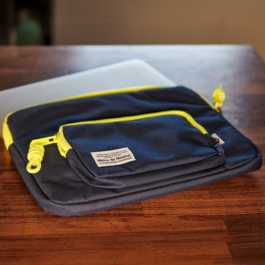 Funda azul con cremalleras amarillas y logo Metro de Madrid sobre mesa de madera