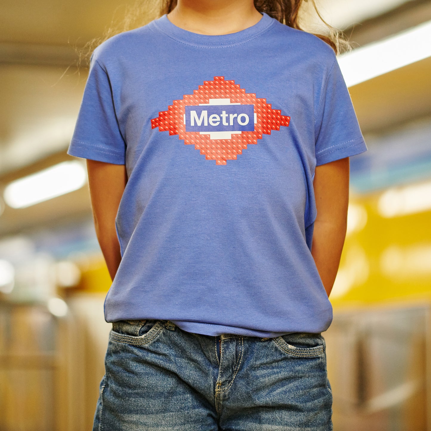 Niña con camiseta azul de logotipo Metro en estación de metro, ropa urbana infantil