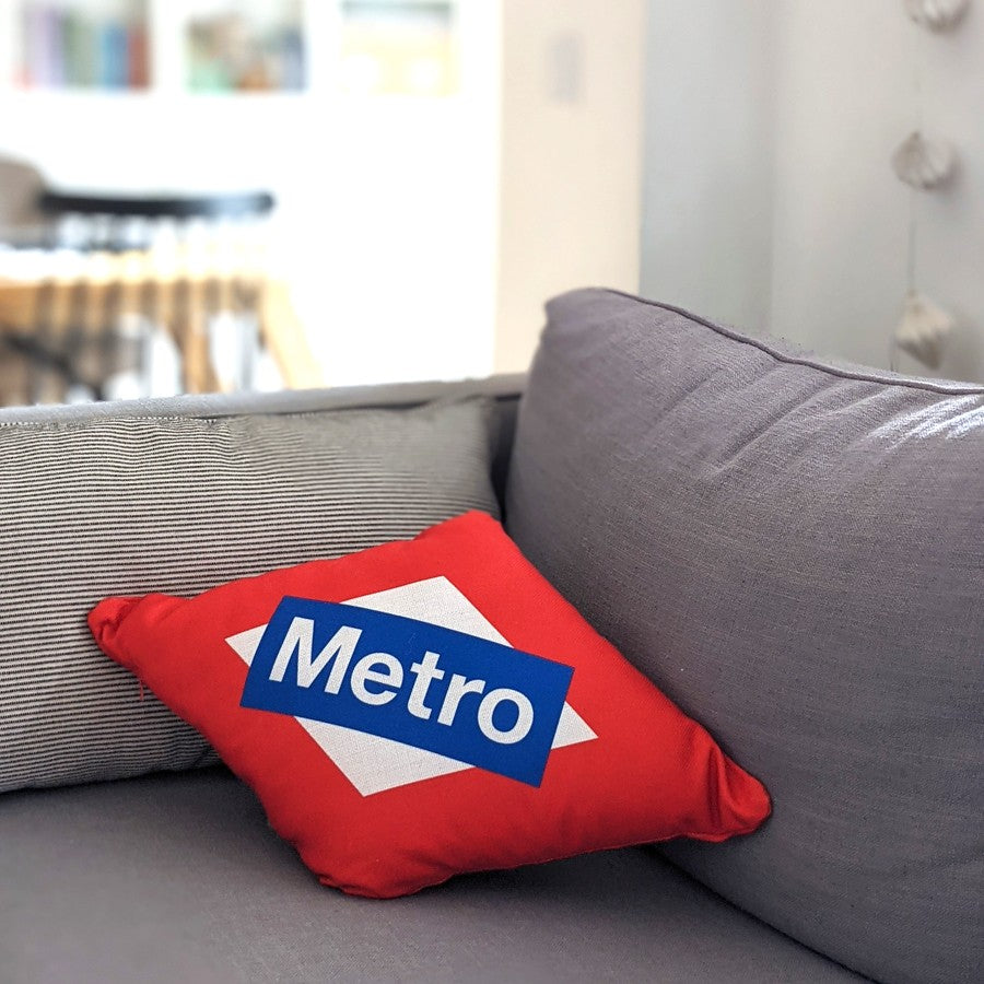Cojín rojo con logo de Metro Madrid sobre sofá gris en sala moderna