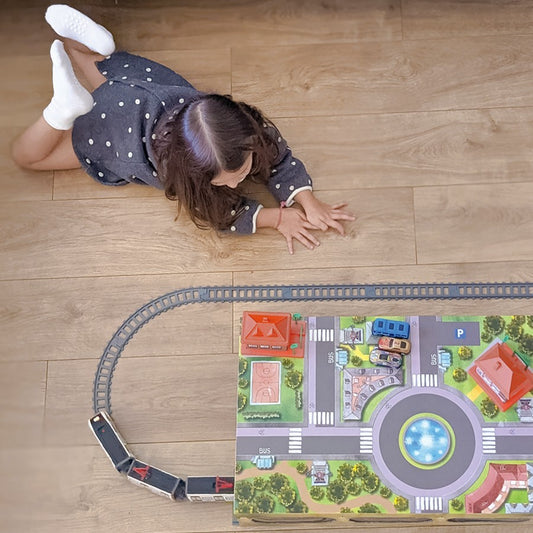 Niña jugando en el suelo con tren de juguete y pista sobre alfombra de ciudad