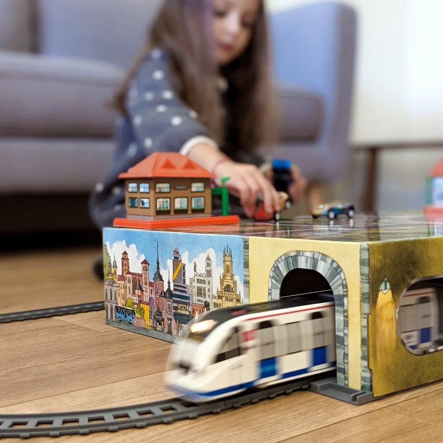 Niña jugando con tren eléctrico de juguete sobre maqueta de ciudad en casa