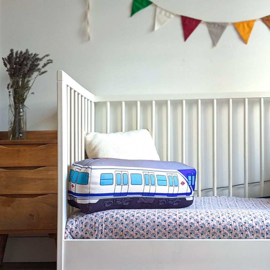 Cojín con forma de metro azul en cuna blanca, fondo de dormitorio infantil decorado.