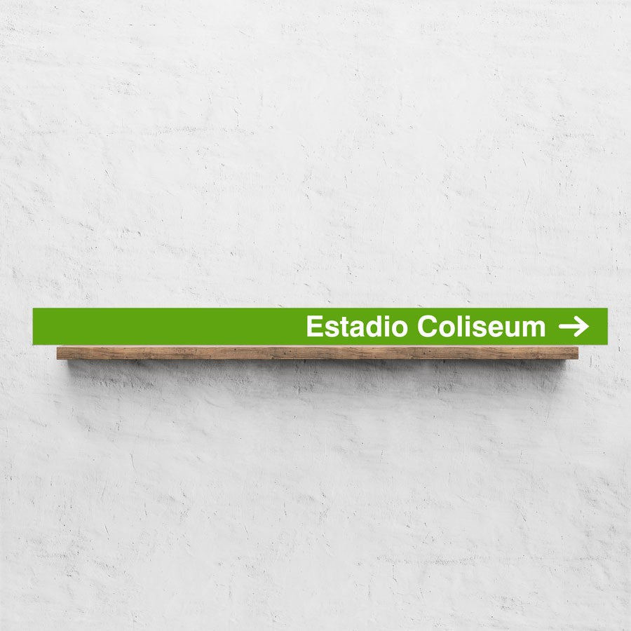 Letrero verde con texto 'Estadio Coliseum' en pared blanca, flecha hacia la derecha