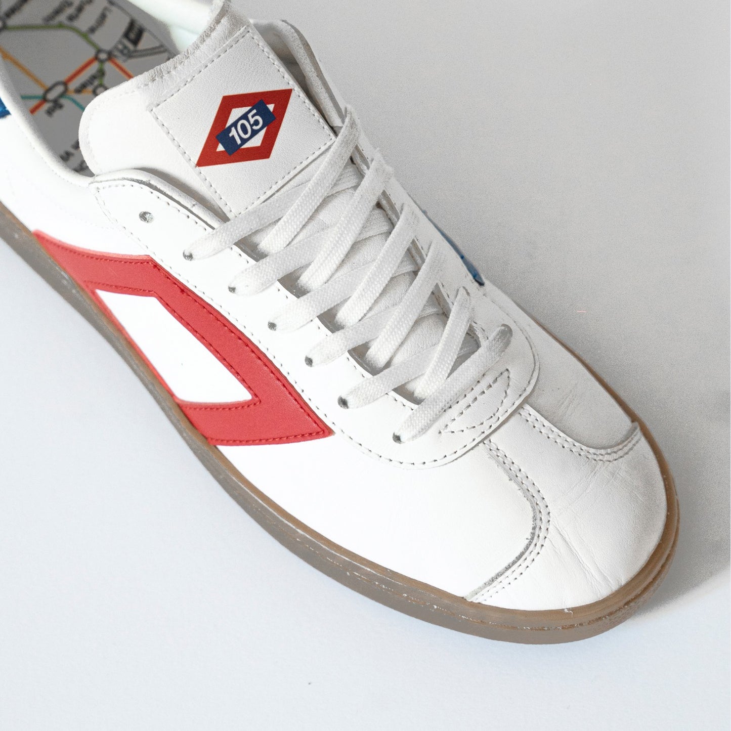 Zapatilla urbana blanca con detalles rojos, diseño de línea de metro y logo 105 en la lengüeta