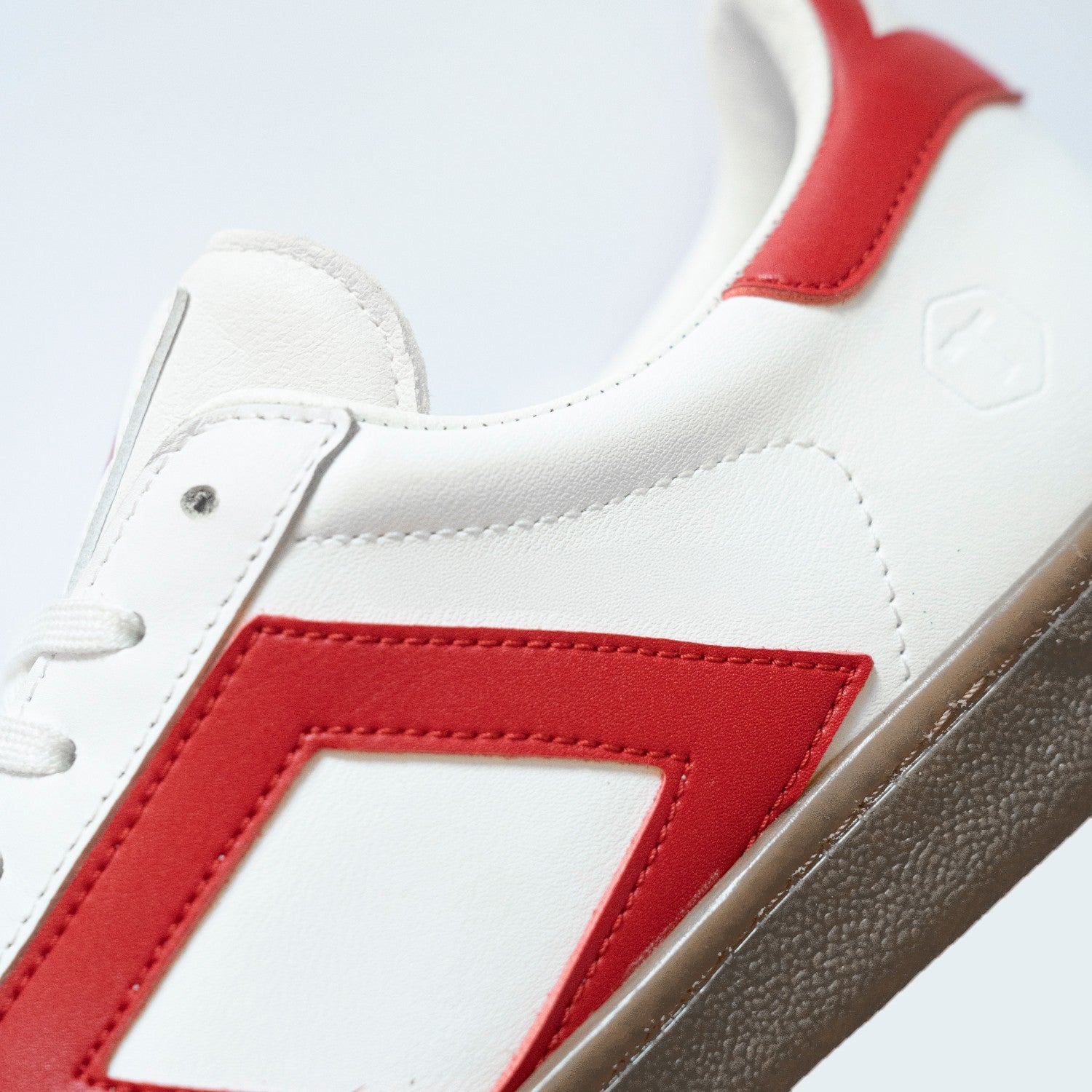 Zapatilla blanca con detalles rojos y suela marrón, vista lateral detallada