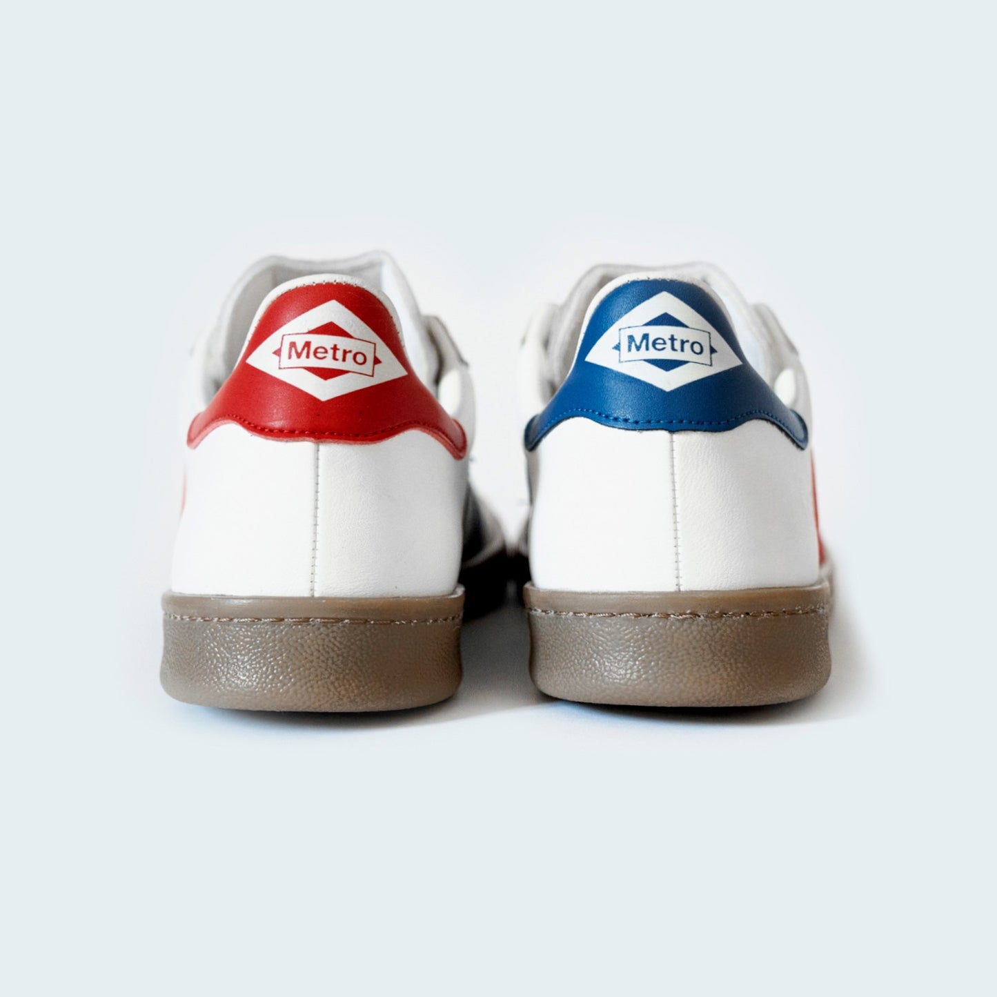 Zapatillas blancas Metro con detalles rojo y azul, fondo claro, vista trasera.