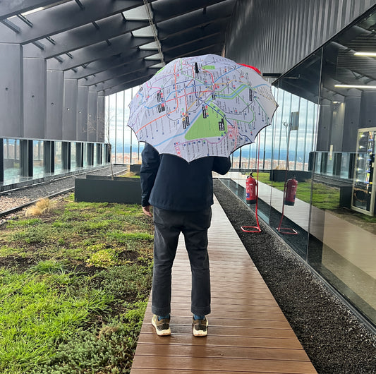 Persona de pie con paraguas de mapa del metro en terraza moderna con jardín y pared de cristal