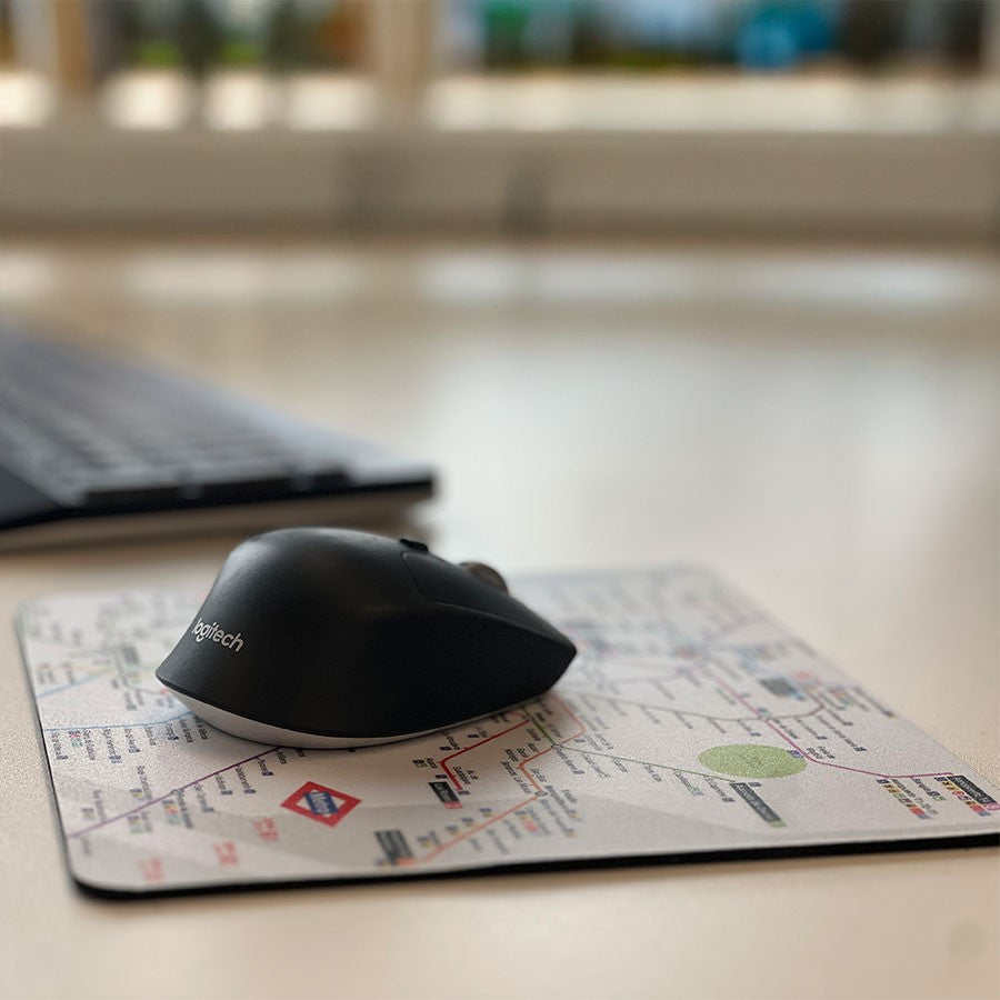 Ratón Logitech negro sobre alfombrilla de mapa del metro en escritorio de oficina moderno