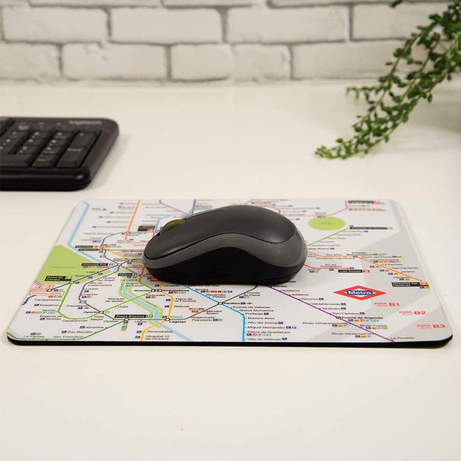 Alfombrilla de ratón con mapa del metro de Madrid, ratón negro y teclado en escritorio blanco.