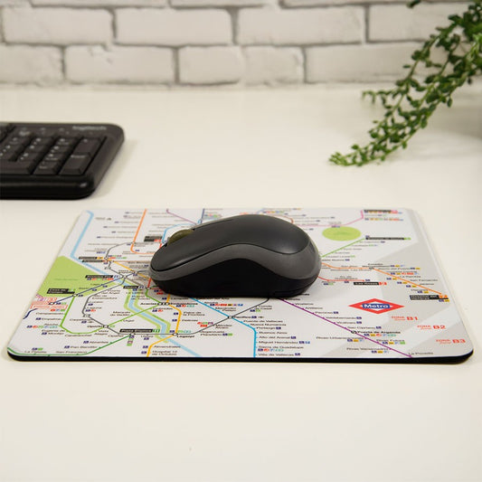Alfombrilla de ratón con mapa del metro de Madrid, ratón negro y teclado en escritorio blanco.
