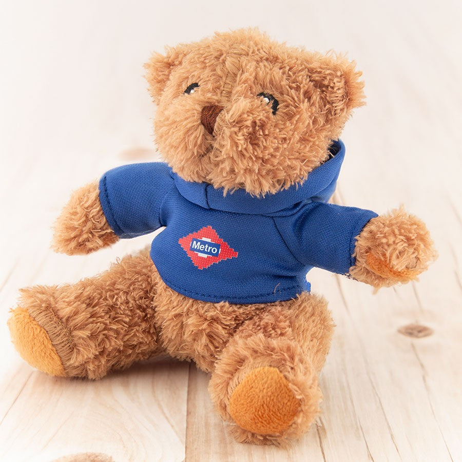 Osito de peluche marrón con sudadera azul de Metro Madrid sobre fondo de madera clara