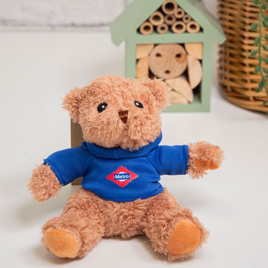 Osito de peluche con suéter azul de Metro Madrid en mesa blanca, fondo decorativo.