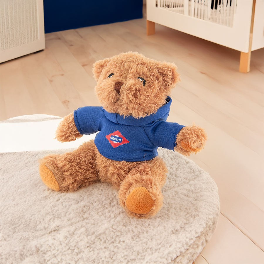 Osito de peluche marrón con sudadera azul de Metro Madrid en habitación infantil luminosa.