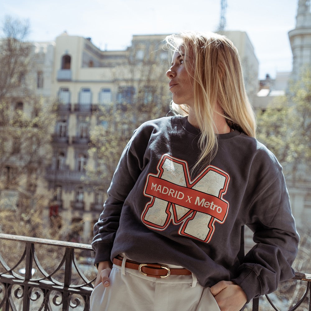 Mujer con sudadera gris Madrid x Metro en balcón urbano, edificios de fondo