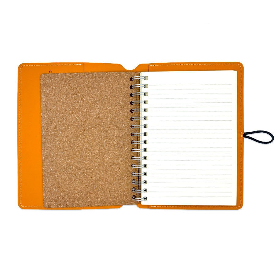 Cuaderno abierto con portada naranja, hojas rayadas y tapa de corcho sobre fondo blanco