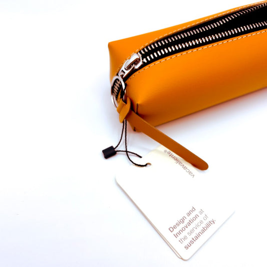 Estuche naranja de cuero vegano con cremallera y etiqueta de sostenibilidad sobre fondo blanco.