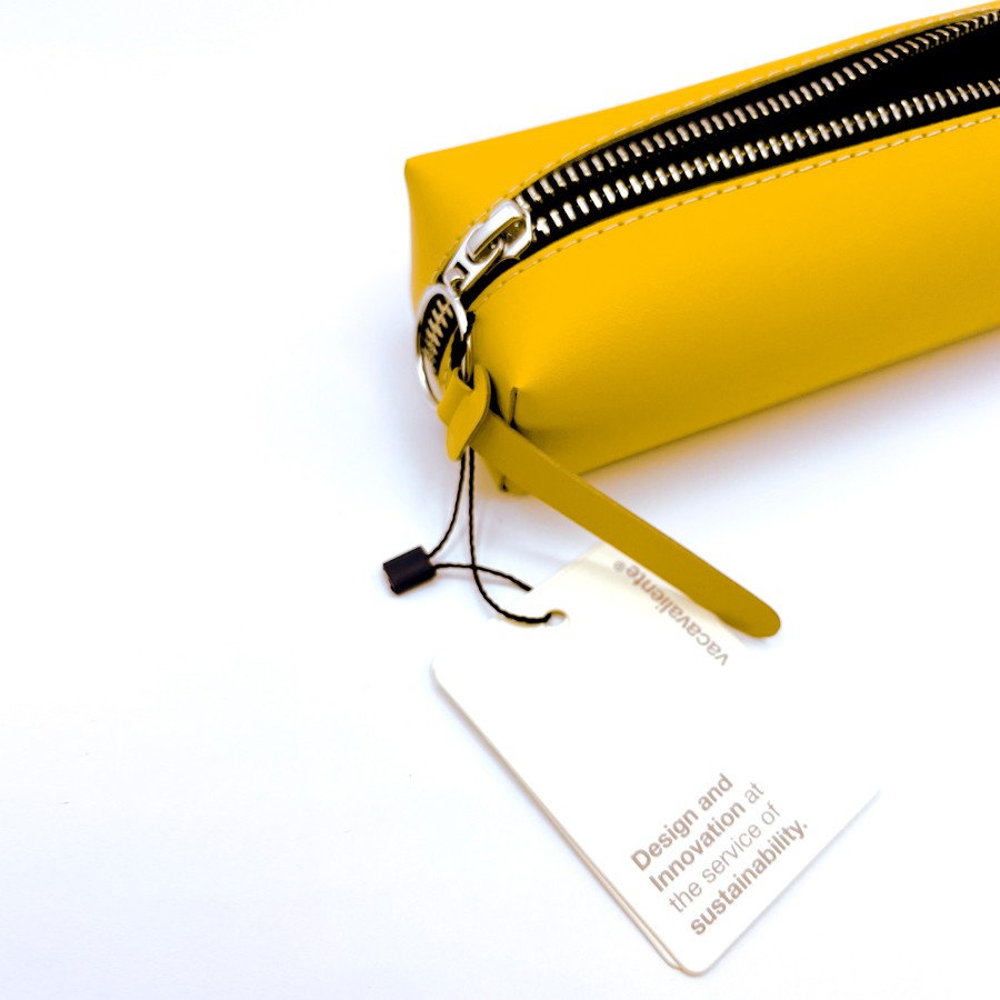 Estuche amarillo con cremallera metálica y etiqueta de sostenibilidad sobre fondo blanco.
