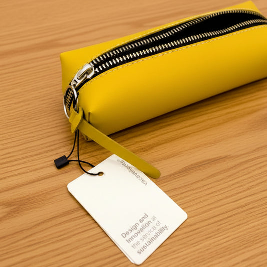 Estuche amarillo con cremallera metálica y etiqueta de sostenibilidad sobre fondo blanco.
