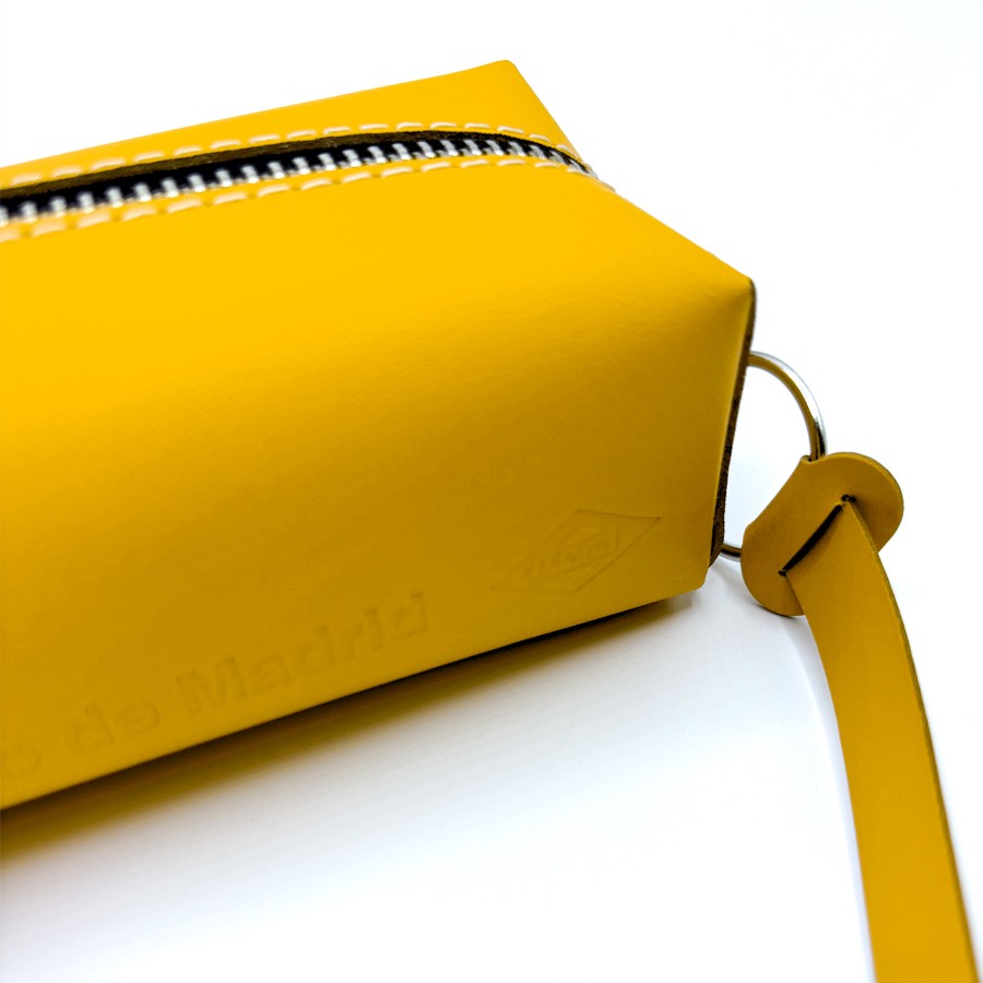 Estuche rectangular amarillo de cuero con cierre metálico, detalle de asa y costuras visibles