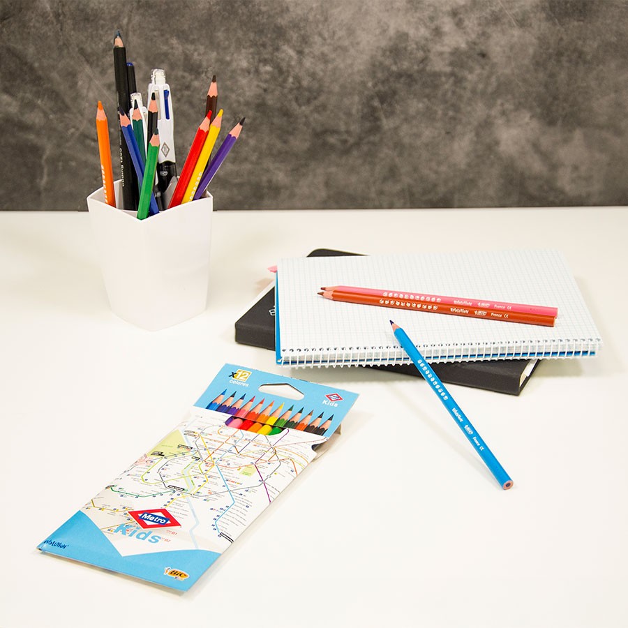 Útiles escolares con lápices de colores, cuadernos y portalápices sobre escritorio blanco