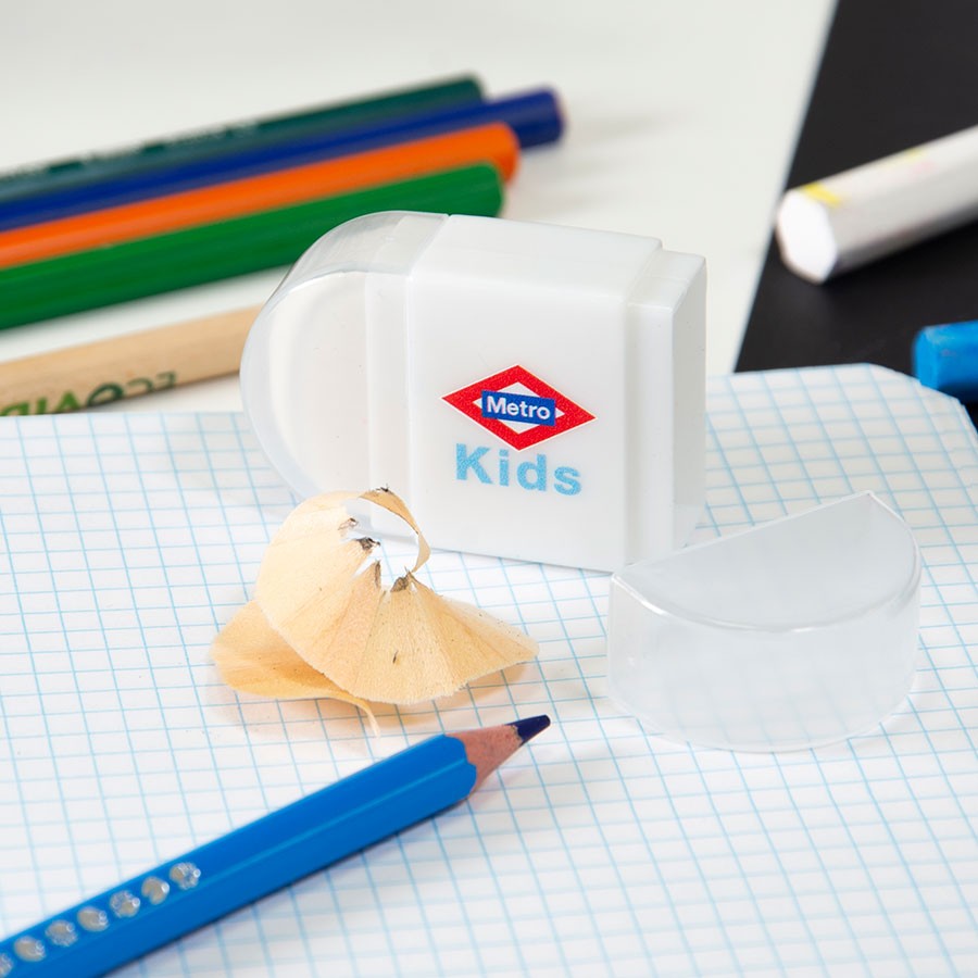 Sacapuntas Metro Kids blanco con lápiz azul sobre cuaderno cuadriculado y útiles escolares.