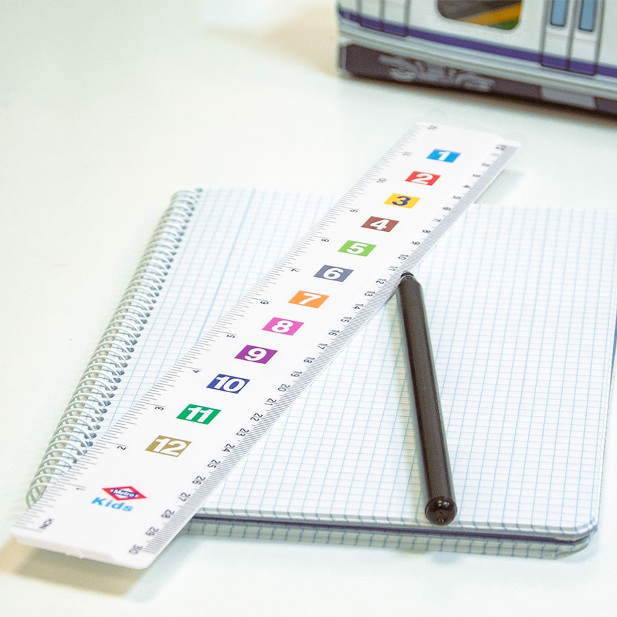 Regla escolar blanca con números de colores, bolígrafo negro y libreta cuadriculada en un escritorio