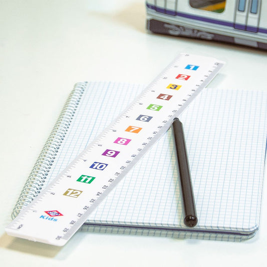 Regla escolar blanca con números de colores, bolígrafo negro y libreta cuadriculada en un escritorio