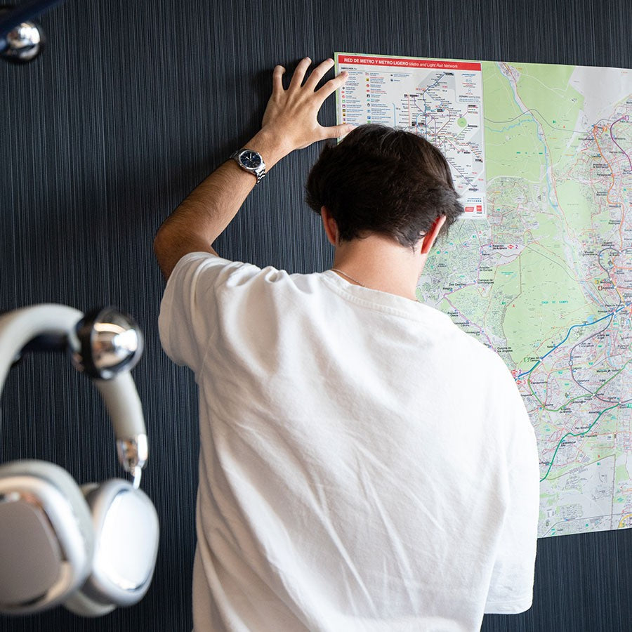 Hombre colocando mapa colorido en pared, auriculares plateados colgados, fondo oscuro