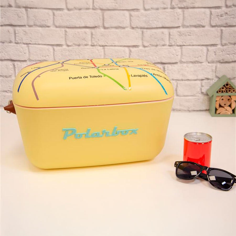 Nevera Polarbox amarilla diseño mapa metro, lata roja y gafas de sol sobre mesa blanca.