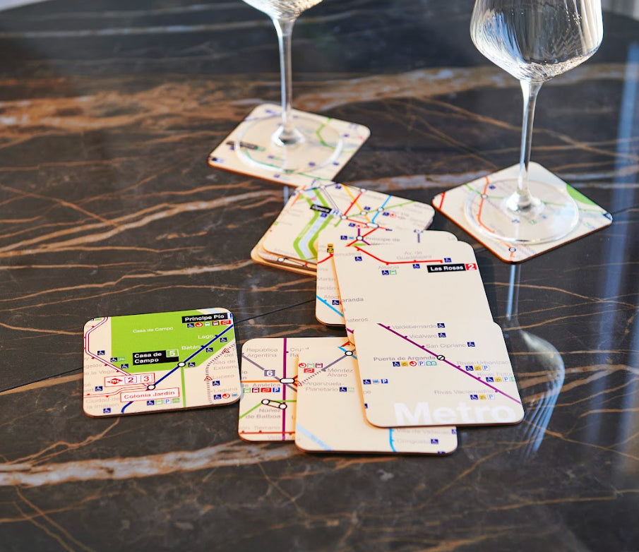 Posavasos con diseño de mapa del metro sobre mesa de mármol, copas de vino.