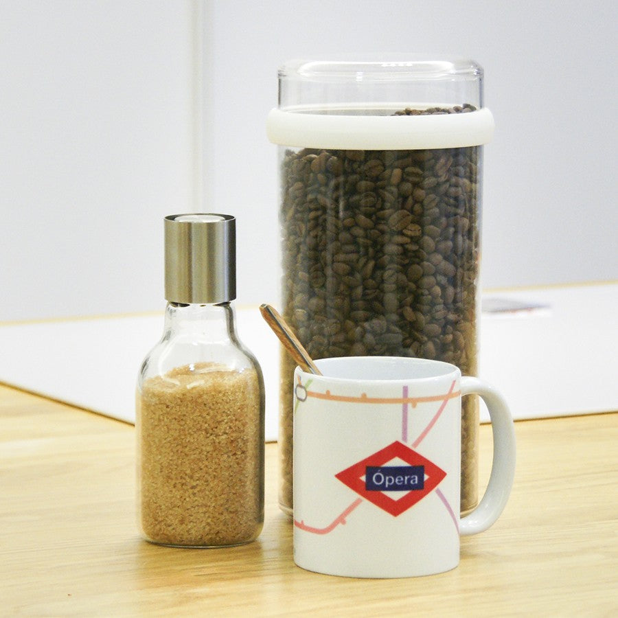 Taza de café Opera, frasco de azúcar y recipiente de granos de café en mesa de madera