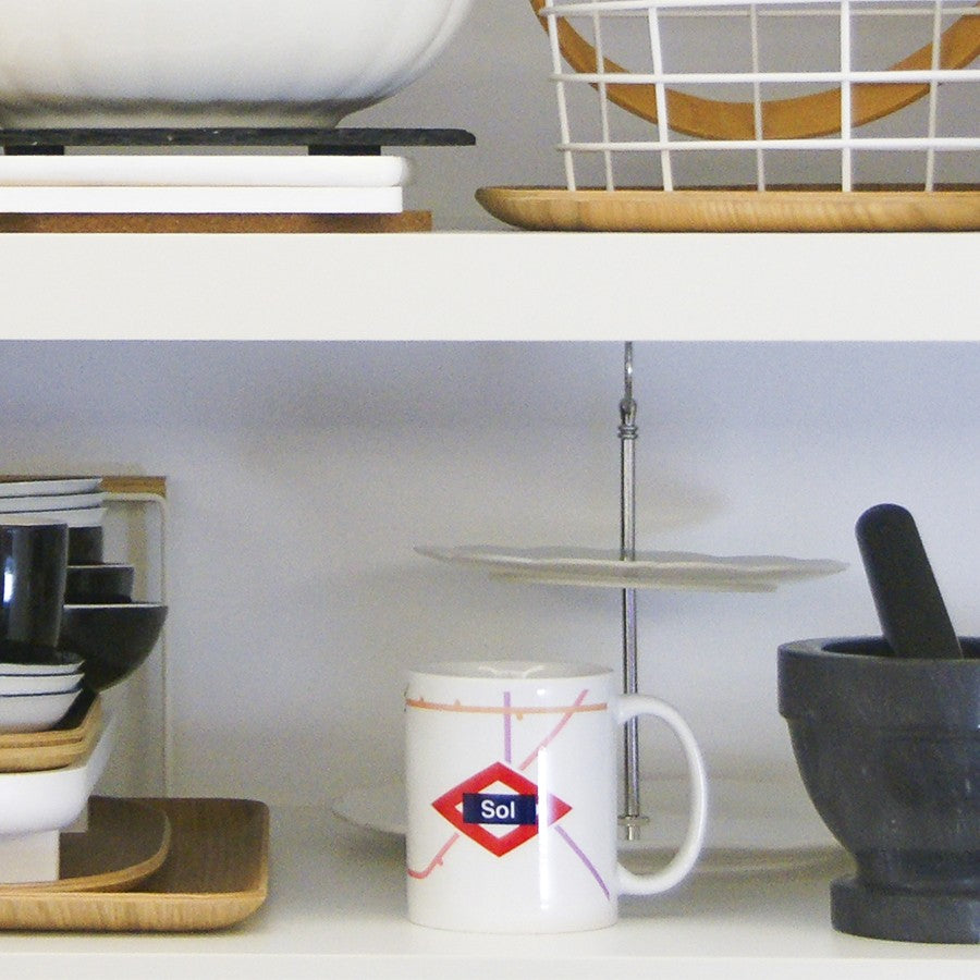 Taza con diseño de metro Sol en estante, mortero negro y vajilla en cocina moderna