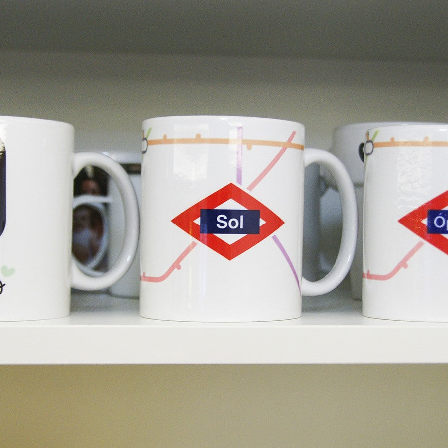 Taza blanca con diseño de estación Sol del metro de Madrid en estante