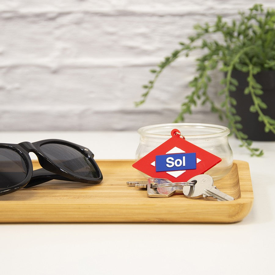 Gafas de sol negras y llavero Sol en bandeja de madera con llaves, fondo con planta