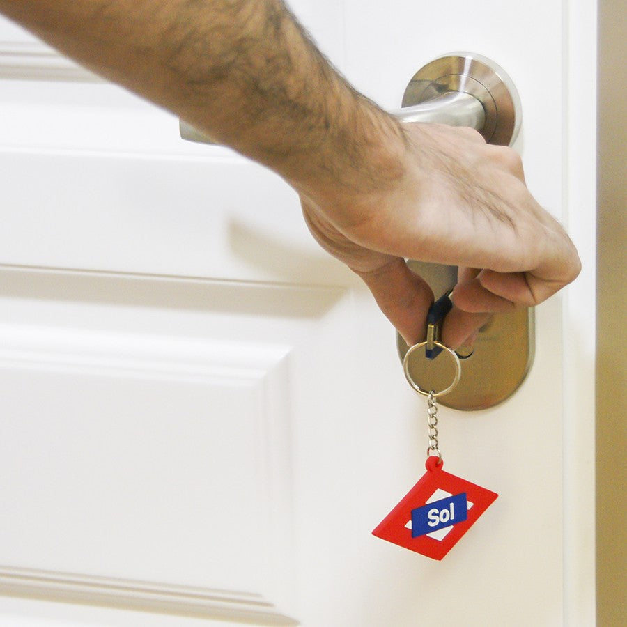 Mano abriendo puerta blanca con llave y llavero rojo de Sol, cerradura metálica moderna.