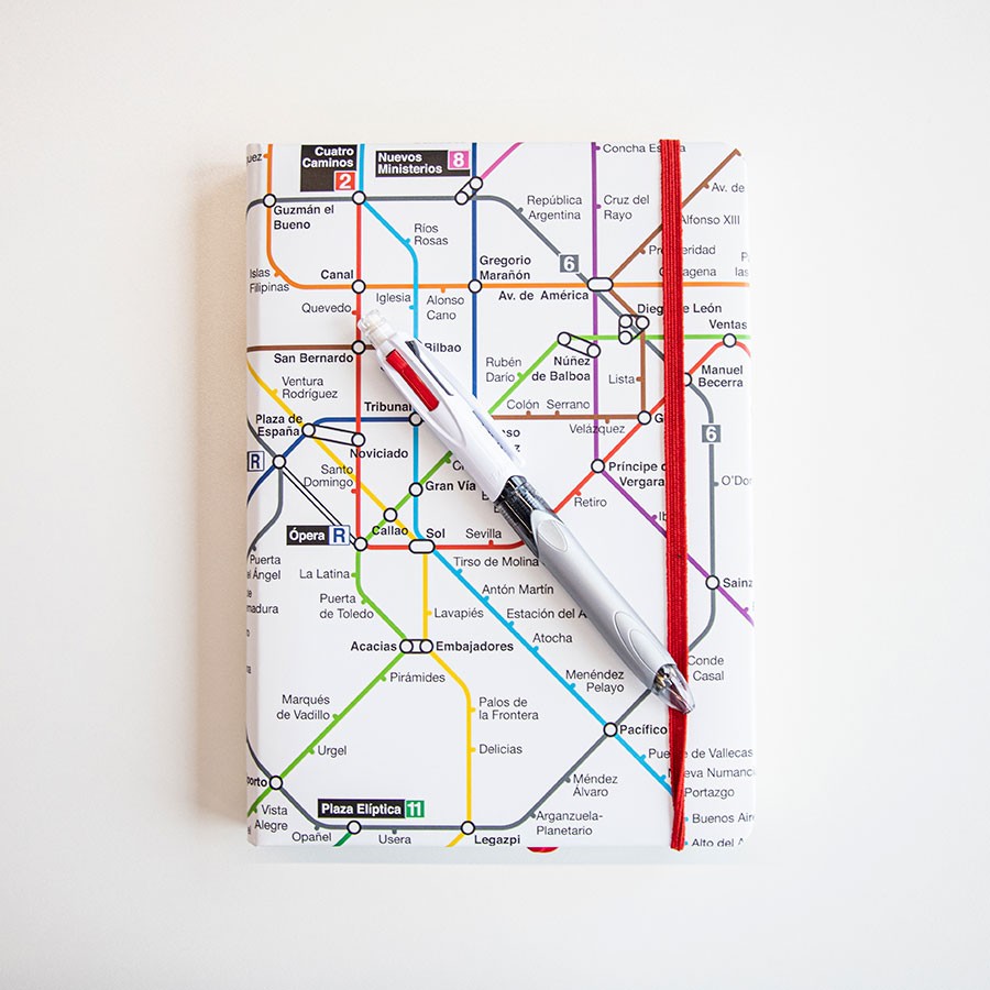 Cuaderno con portada de mapa del metro de Madrid y bolígrafo multicolor sobre fondo blanco