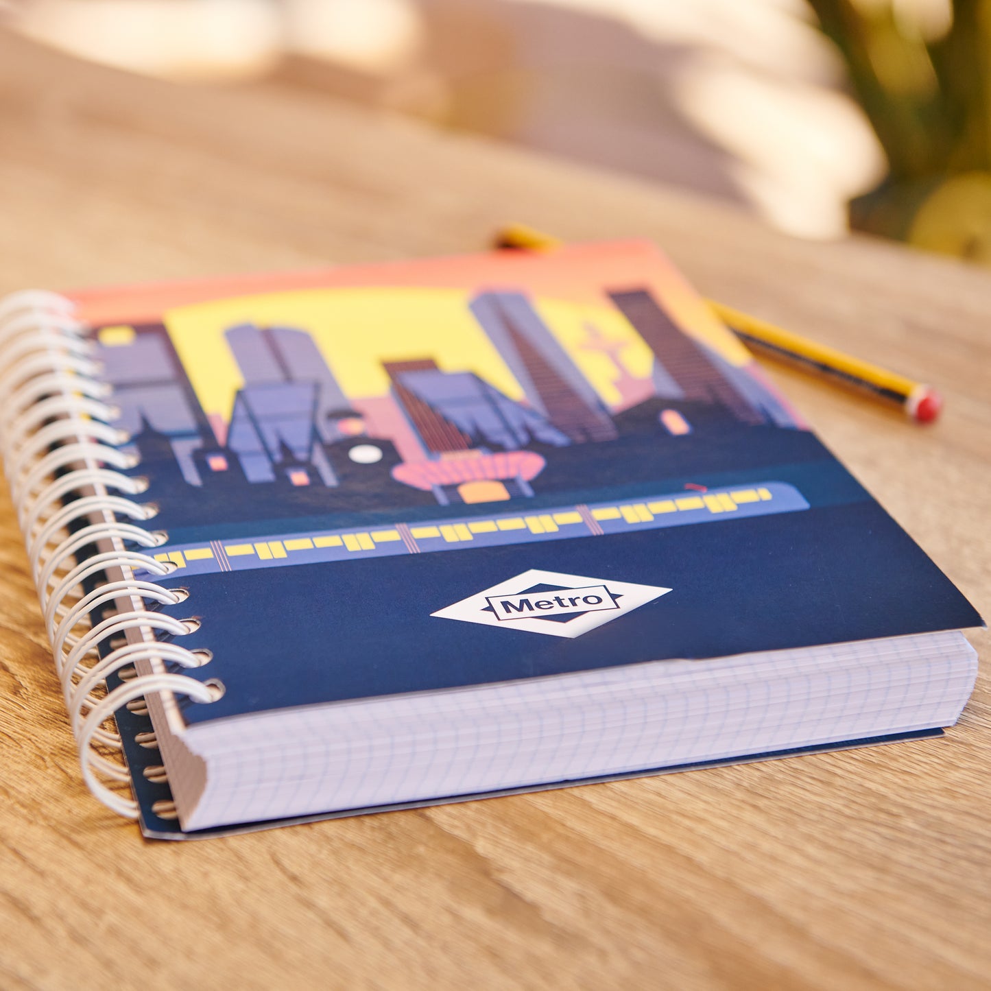 Cuaderno de espiral Metro con portada de ciudad al atardecer sobre mesa de madera.