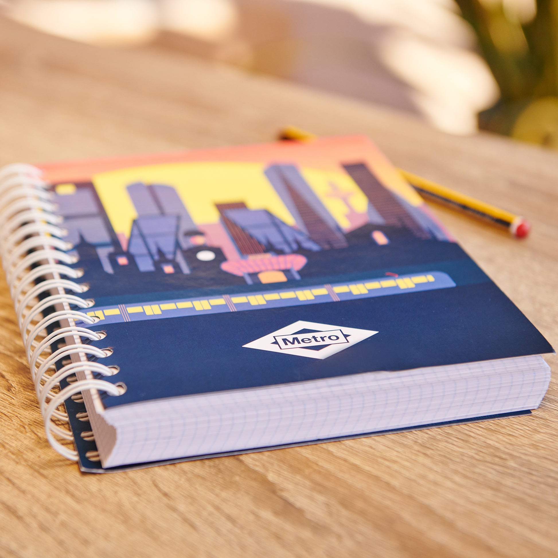 Cuaderno de espiral Metro con portada de ciudad al atardecer sobre mesa de madera.
