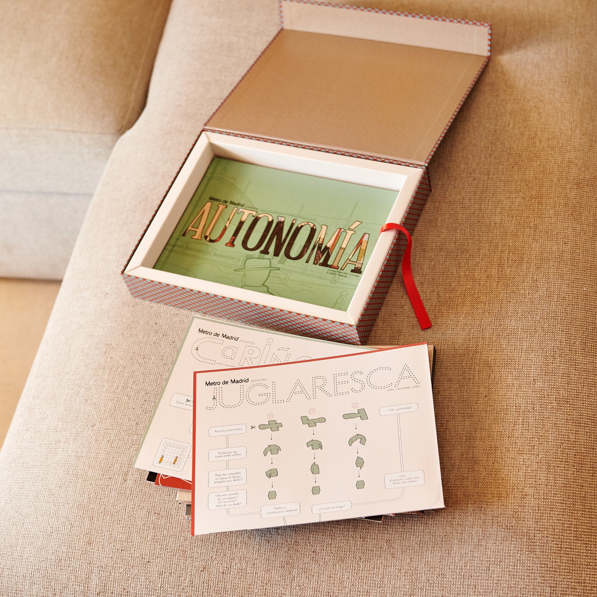 Caja regalo con libro 'Autonomía' y láminas educativas sobre el Metro de Madrid en un sofá