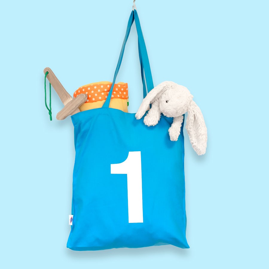 Bolsa azul infantil con número uno, peluche de conejo y juguetes sobre fondo celeste