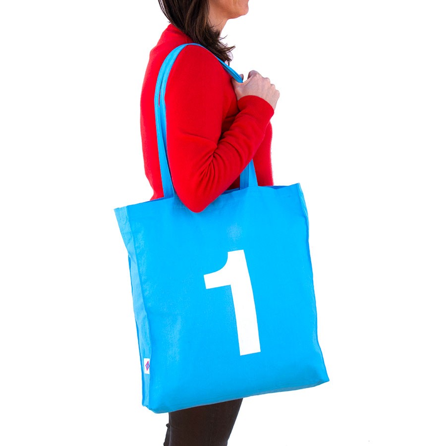 Bolsa azul de tela reutilizable con número uno grande impreso, mujer la lleva al hombro.