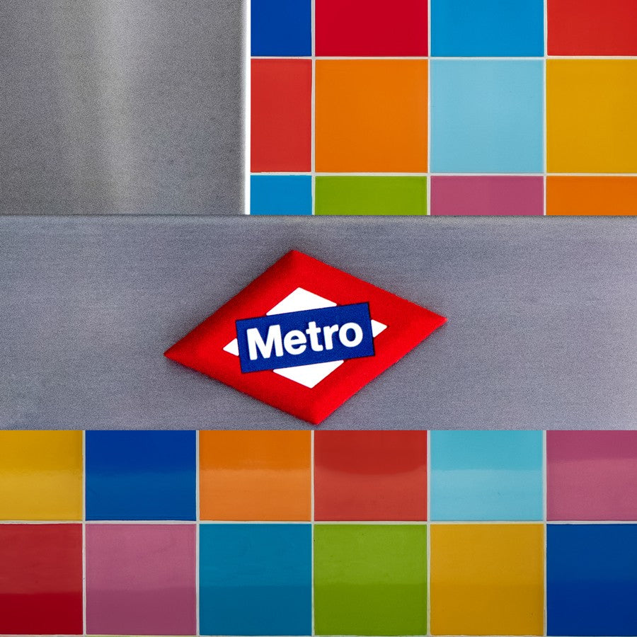 Logo del Metro en forma de rombo rojo sobre fondo de azulejos coloridos.