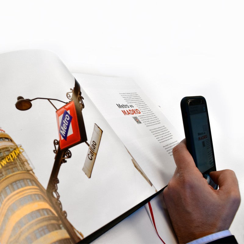 Persona usando móvil sobre libro abierto del Metro de Madrid, estación Callao.