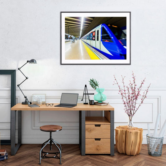 Oficina moderna con escritorio de madera, portátil y cuadro de metro azul en la pared